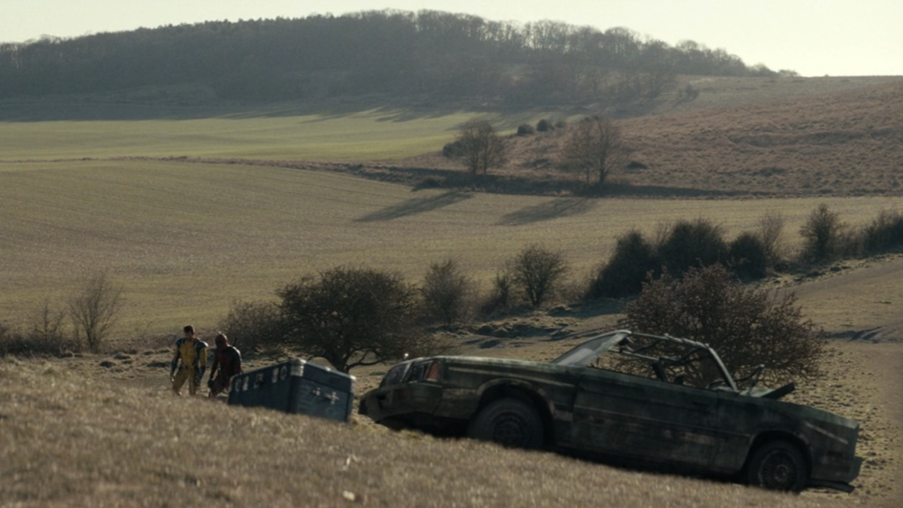 Deadpool &amp; Wolverine walk in The Void near a burnt out car.