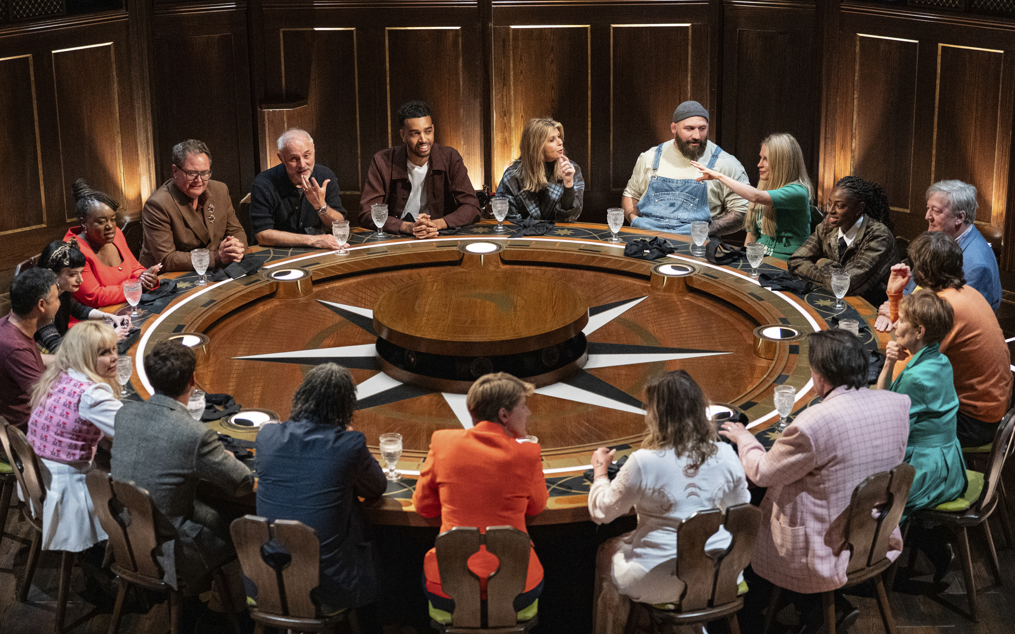 Twenty people, many of whom are celebrities, sit around a large, circular wooden table in "The Celebrity Traitors."