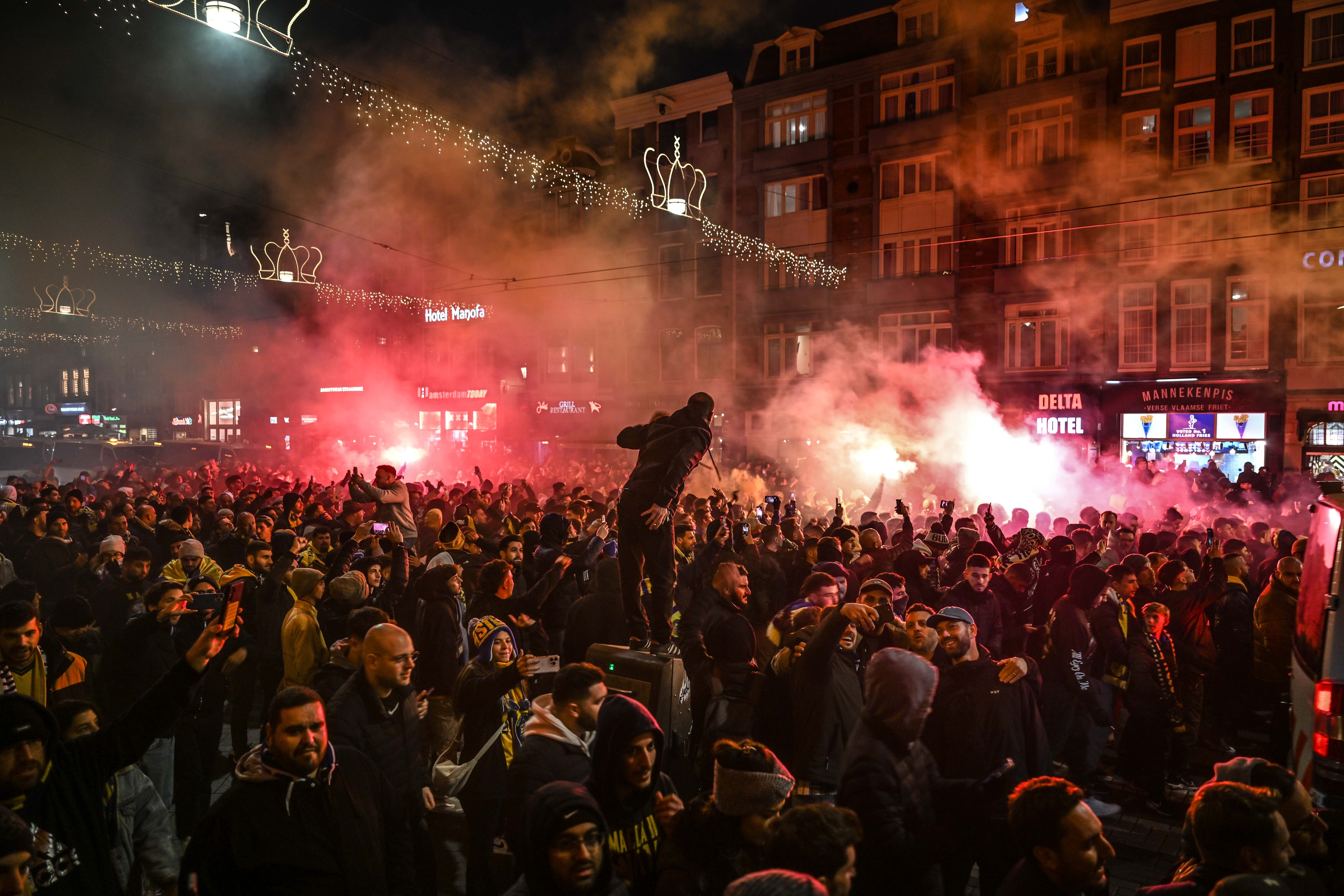Pro-Israel Maccabi fans demonstrating in Dam Square, Amsterdam, with flares and smoke filling the air.