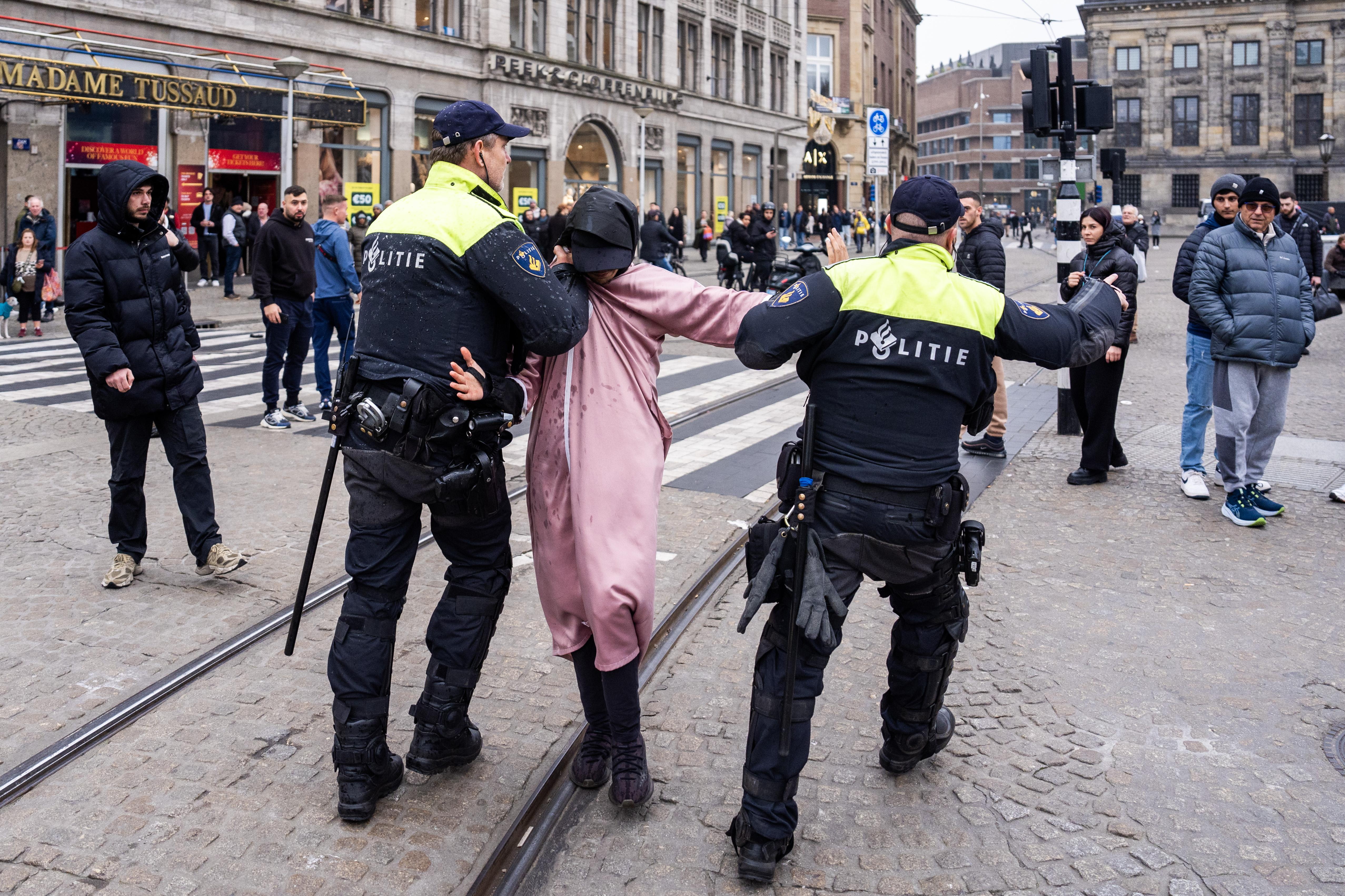 Two Dutch police officers detain a man on a cobblestone street in Amsterdam.