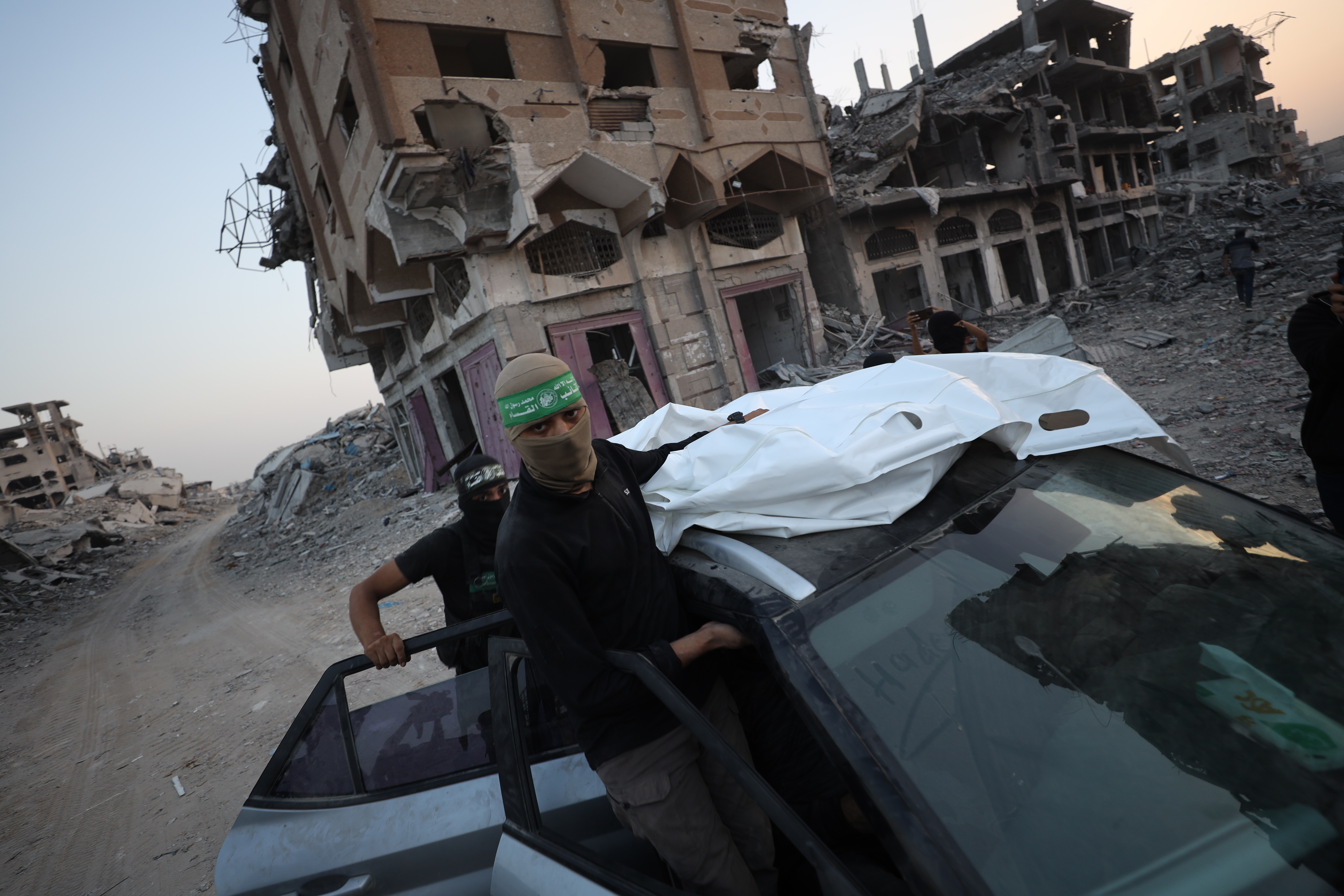 Members of Hamas with a covered body in front of collapsed buildings in Gaza.