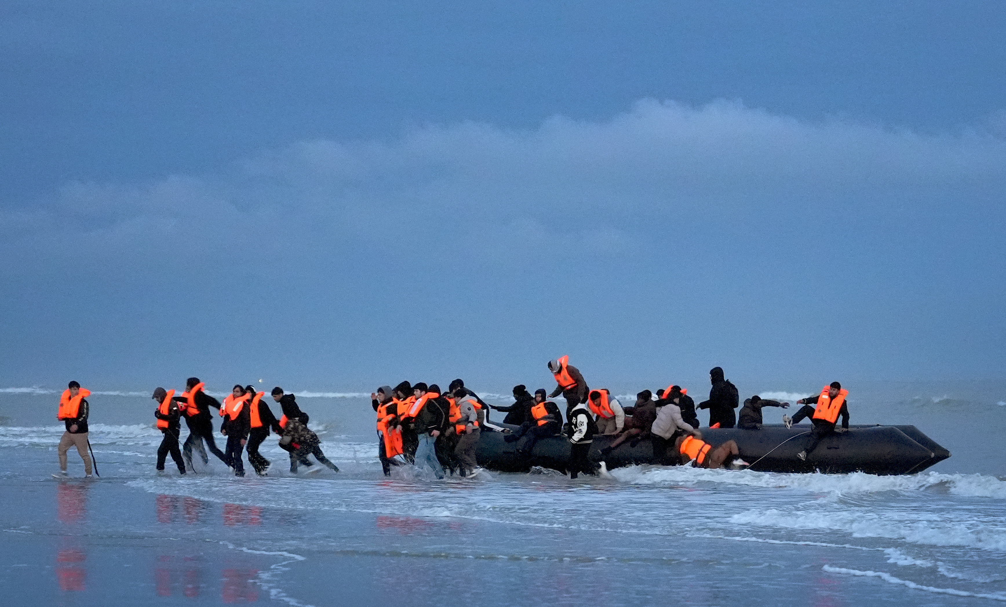 People believed to be migrants flee a deflating small boat after attempting to cross the Channel in Gravelines, France.
