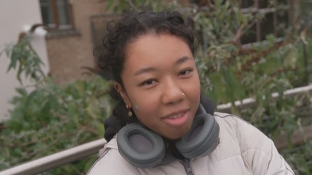 Renna Nakyama stands in front of a hedge.