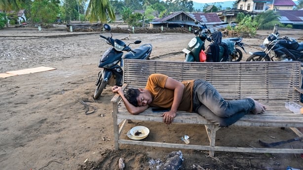 A man sleeps on a bench with motorbikes in the background