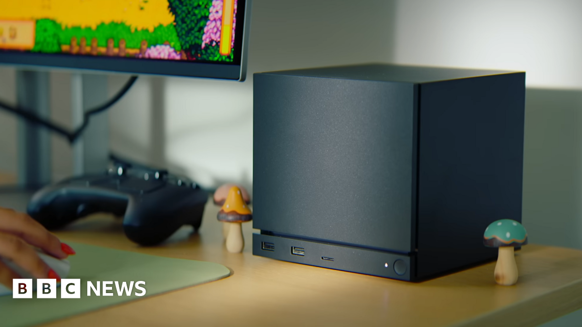 A large black cube sits on a desk. It has a strip cut out near the bottom, below which is a power button and three USB ports.