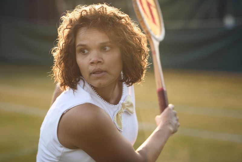 Female tennis player preparing to serve on a grass court, showcasing determination and focus in her athletic attire.