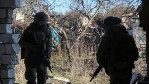 Reuters Soldiers stand with guns besiude a ruined building. 