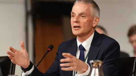 PA Media Tim Davie speaks while sitting wearing a suit and tie.