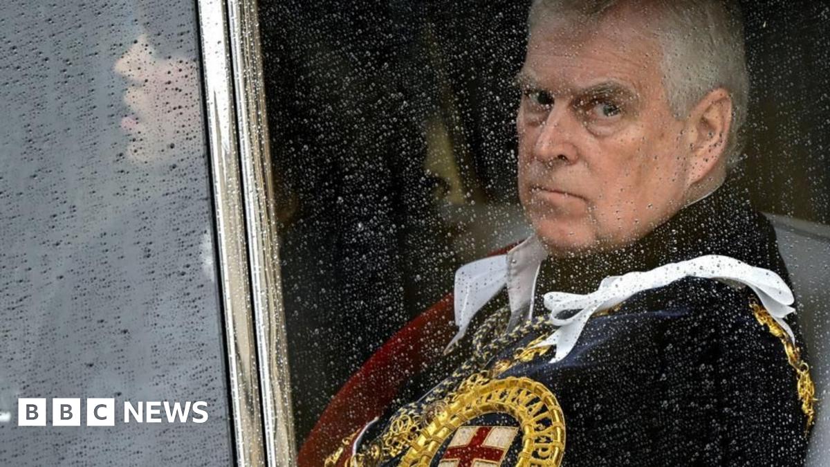 Prince Andrew sitting behind a glass window in a car with raindrops on it. He is looking glum and wearing a royal uniform with golden trim and a St George's cross on it.