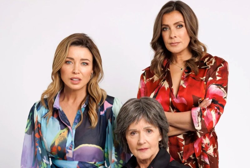 Three women pose for a portrait, showcasing vibrant fashion choices. The woman in the foreground has short, grey hair and a confident expression, while the two women behind her display long, styled hair and striking outfits in bold colours. The image highlights themes of empowerment and diversity in women's fashion.