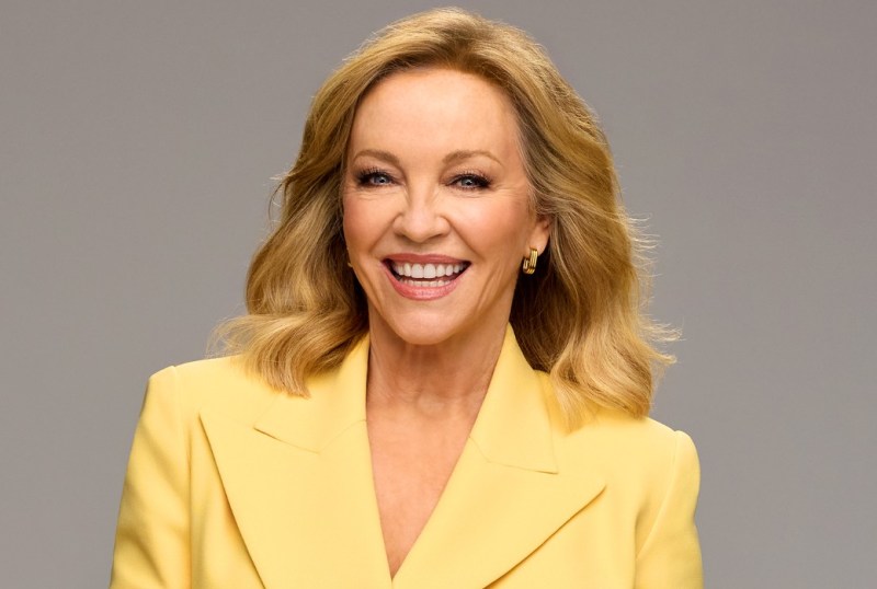 Smiling woman with blonde hair wearing a bright yellow blazer against a neutral background, showcasing a cheerful and confident expression.