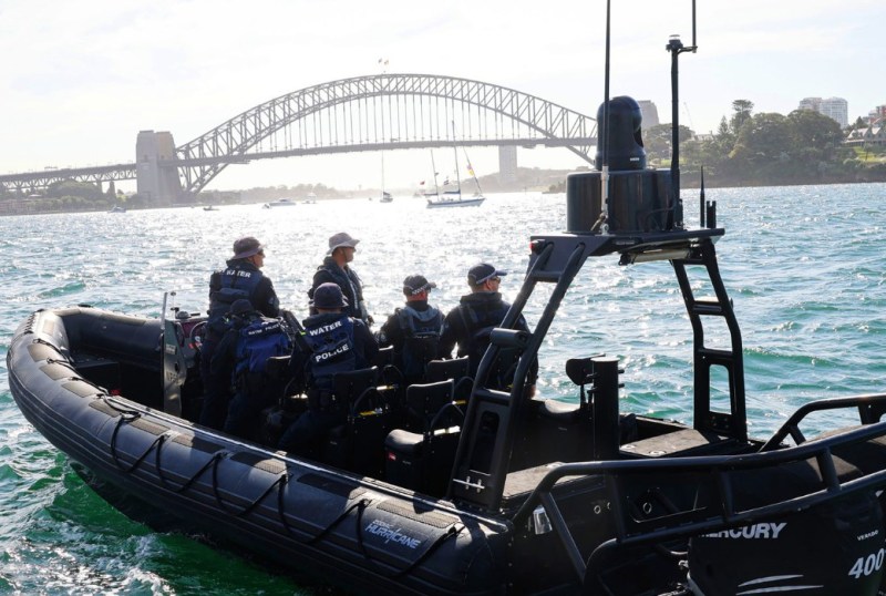 Water police officers on a patrol boat in Sydney Harbour, with the Sydney Harbour Bridge in the background and boats on the water.