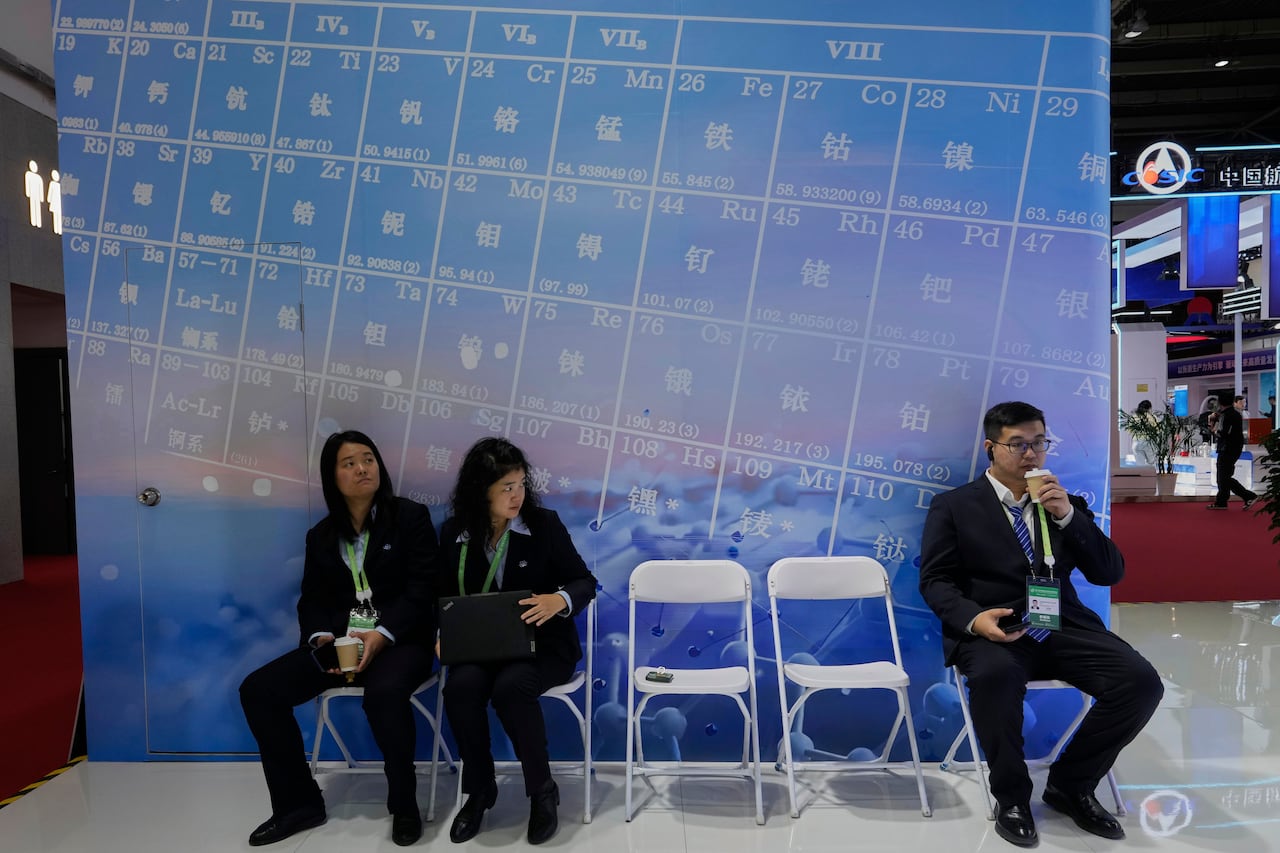 People sit on white folding chairs in front of a blue backdrop.
