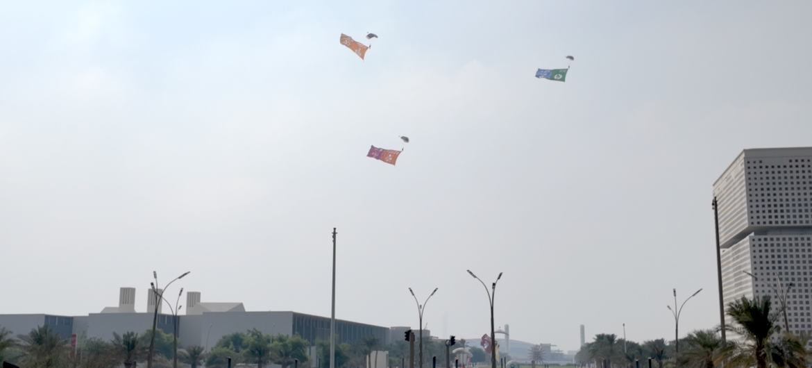 A Qatari parachute team performs an aerial display, descending over the QNCC while carrying the 17 colourful Sustainable Development Goal flags, alongside the UN and Qatari flags.