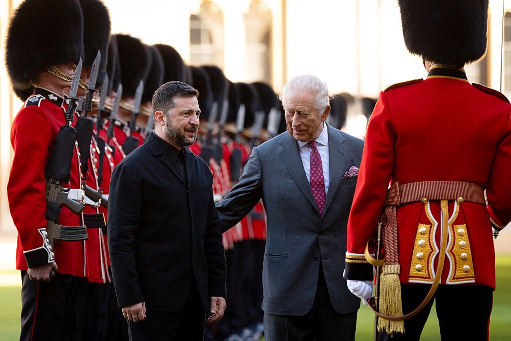 Two people stand in front of people in military uniforms.