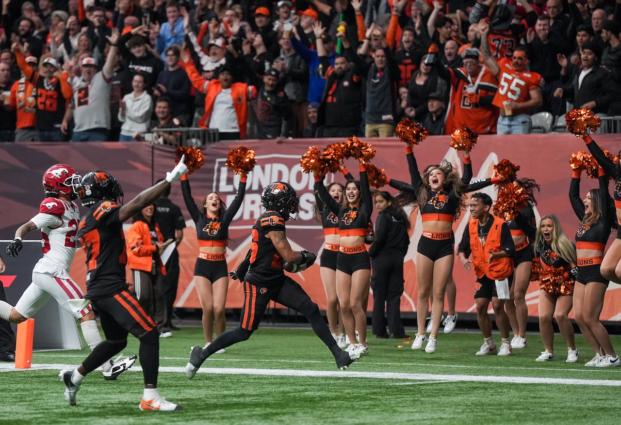 Cheerleaders celebrate as a football player points to the sky in the endzone