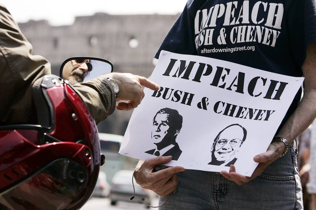 A person holds a piece of paper that reads, 'Impeach Bush and Cheney.'