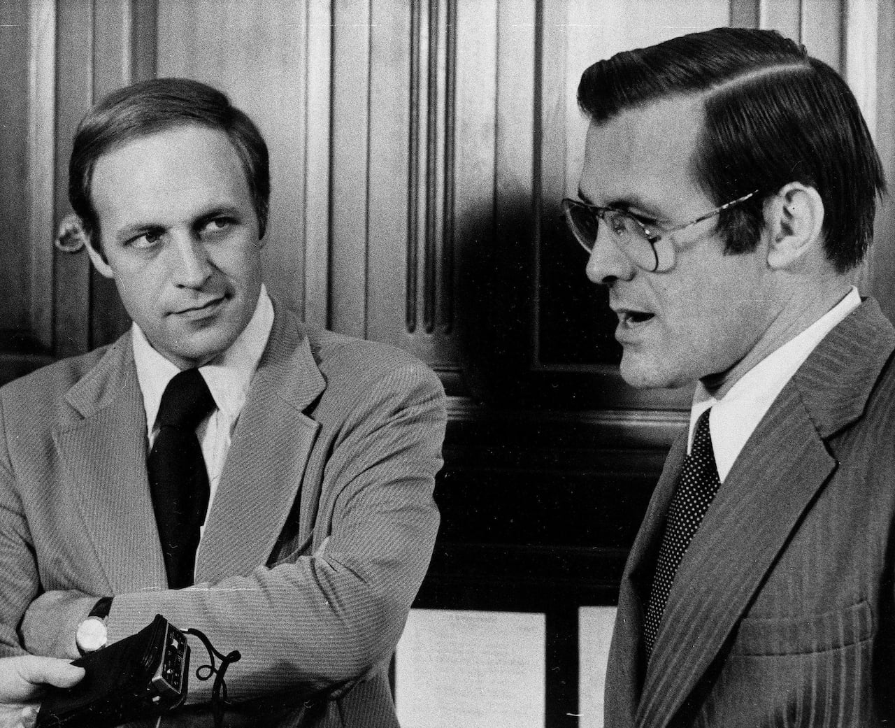 Two cleanshaven men in suit and tie are shown next to each other in a black and white photograph, one is bespectacled.