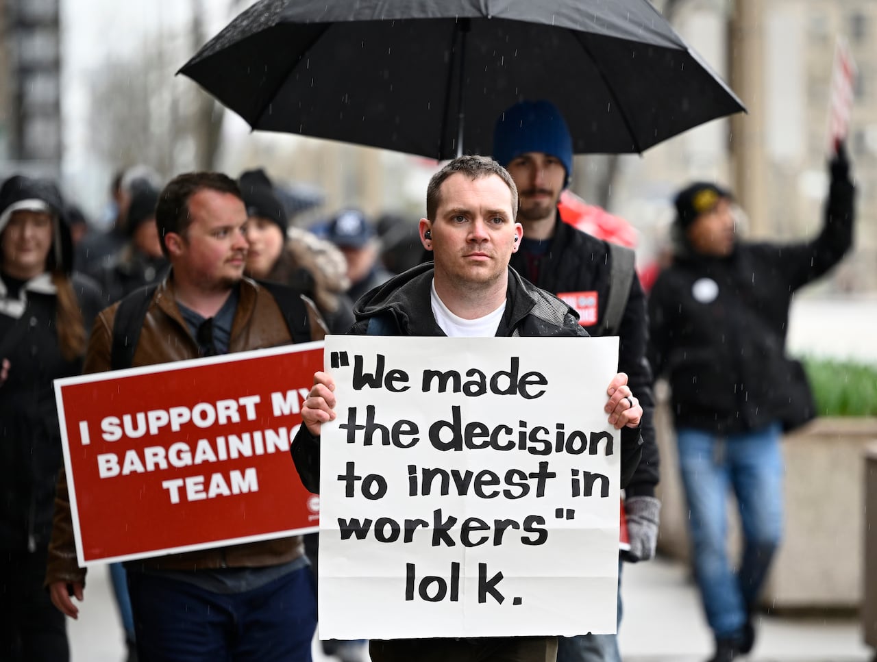 Public servants with PSAC walk on a picket line outside the prime minister's office holding up a sign that reads: "We made the decision to invest in workers lol k."