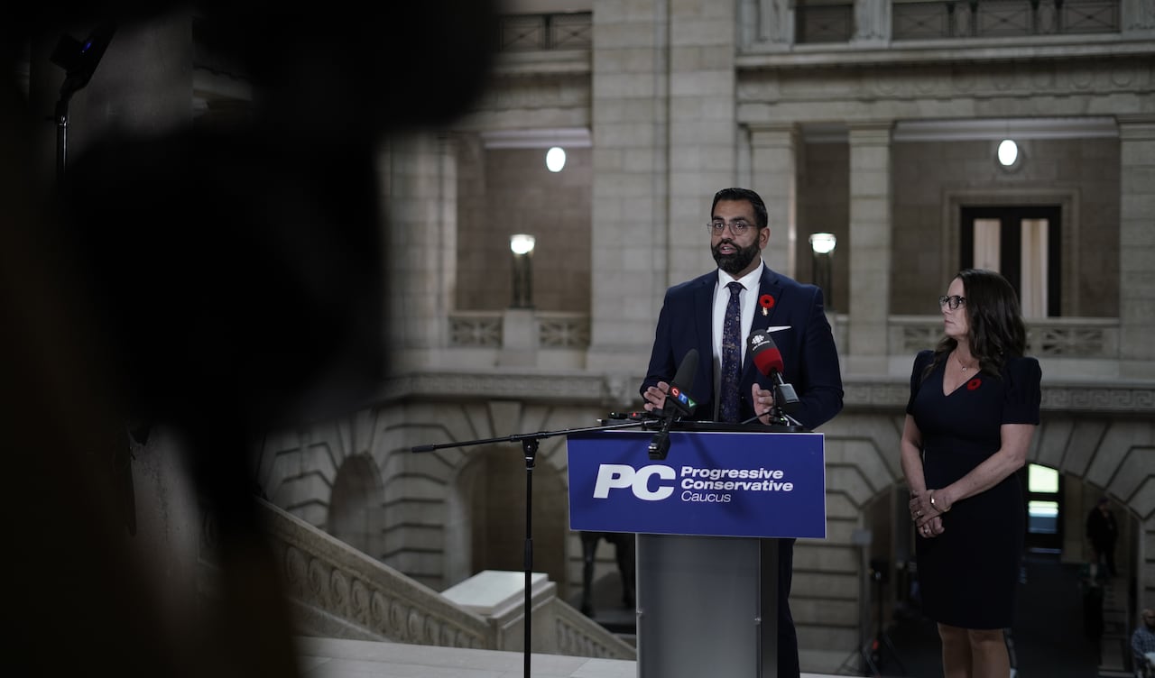 A man in a suit and woman in a dress speak from behind a lectern.