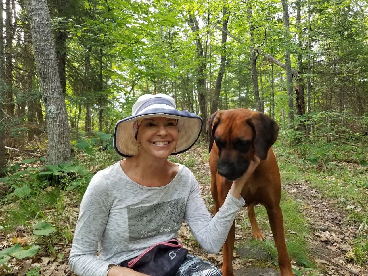 A woman during cancer treatment with a dog and trees behind her.
