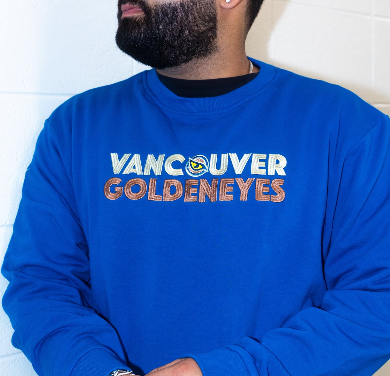 A man is shown wearing a blue sweater with a logo on it.