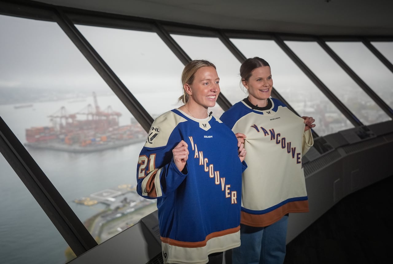Two women are standing in front of a window and wearing Vancouver hockey jerseys