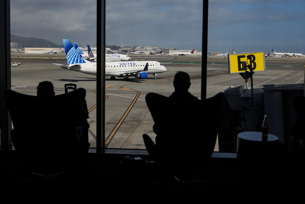 A silhouette of people sitting in chairs in front of an  airport window