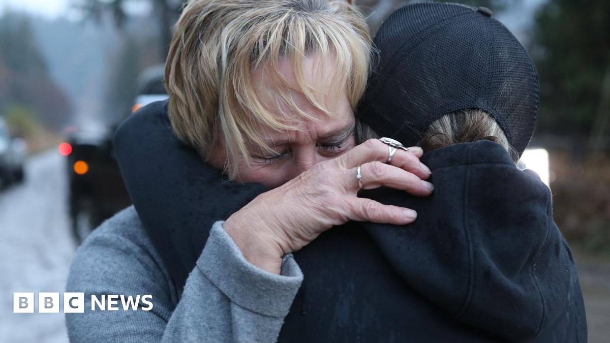 A group of ostrich supporters, in rain gear, hold hands and cry