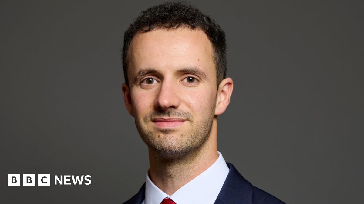 Chris Hinchliff wearing a suit with a white shirt and red tie. He is looking directly at the camera and smiling.
