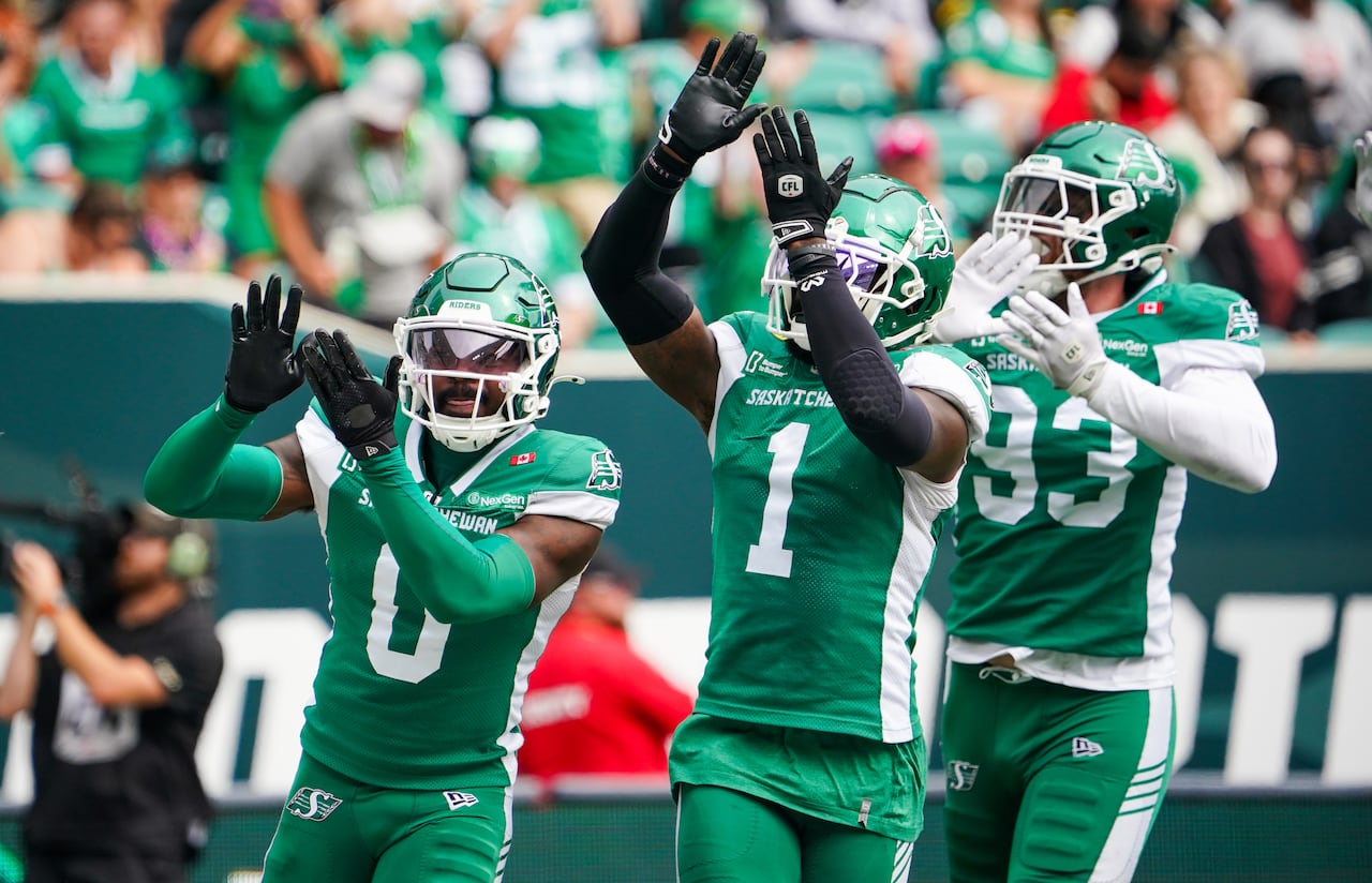 Three football players in green jerseys are seen playing on the field. 