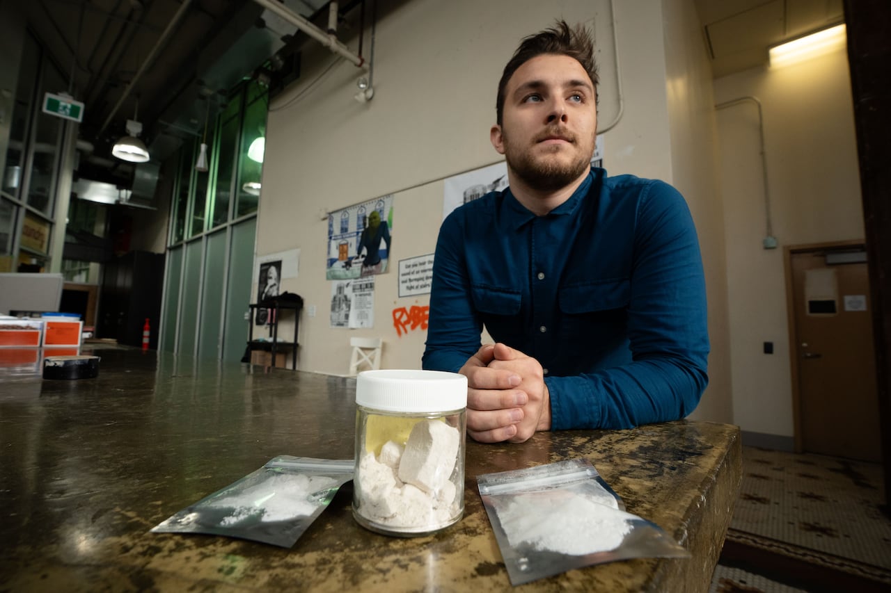 A man is pictured sitting at a table with white substances in baggies and a jar in front of him.