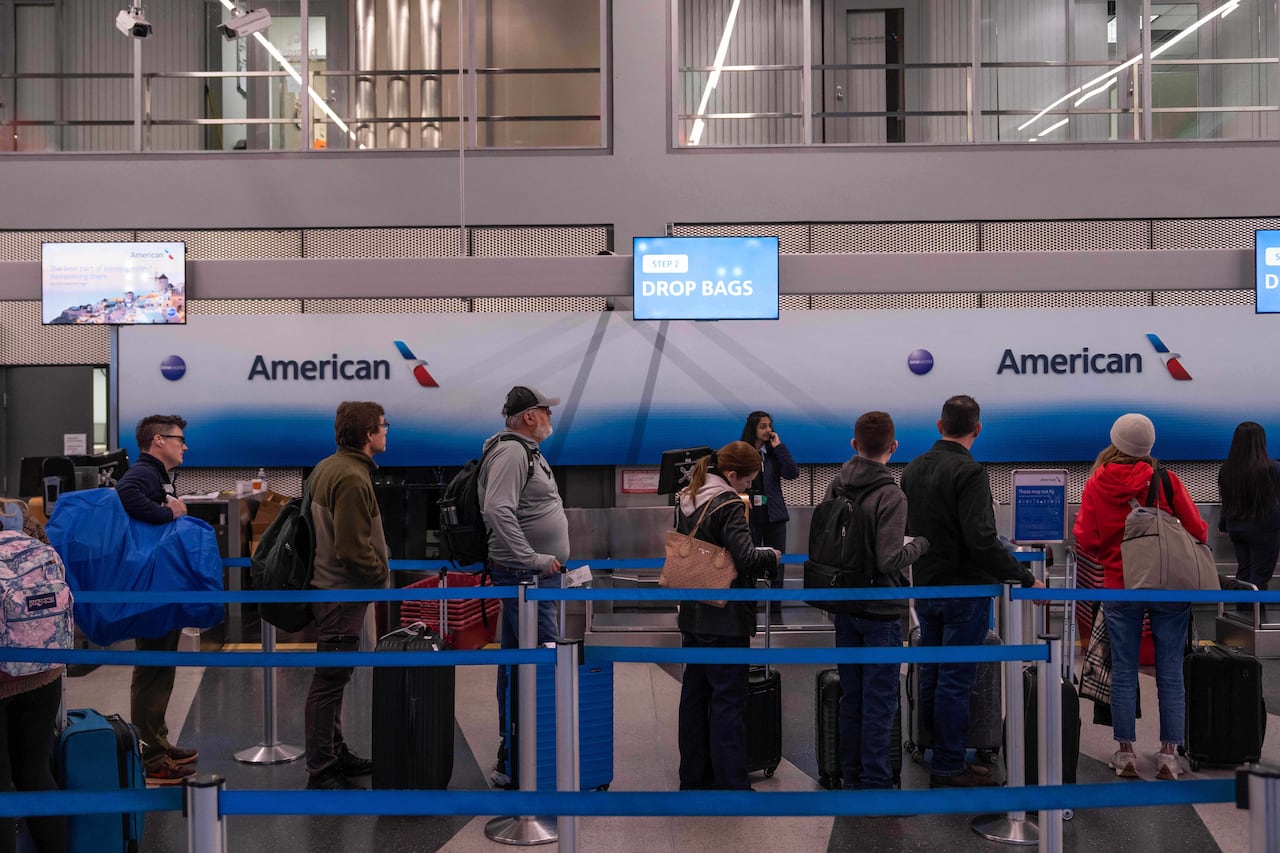 People wait in line with their luggage at an airport.