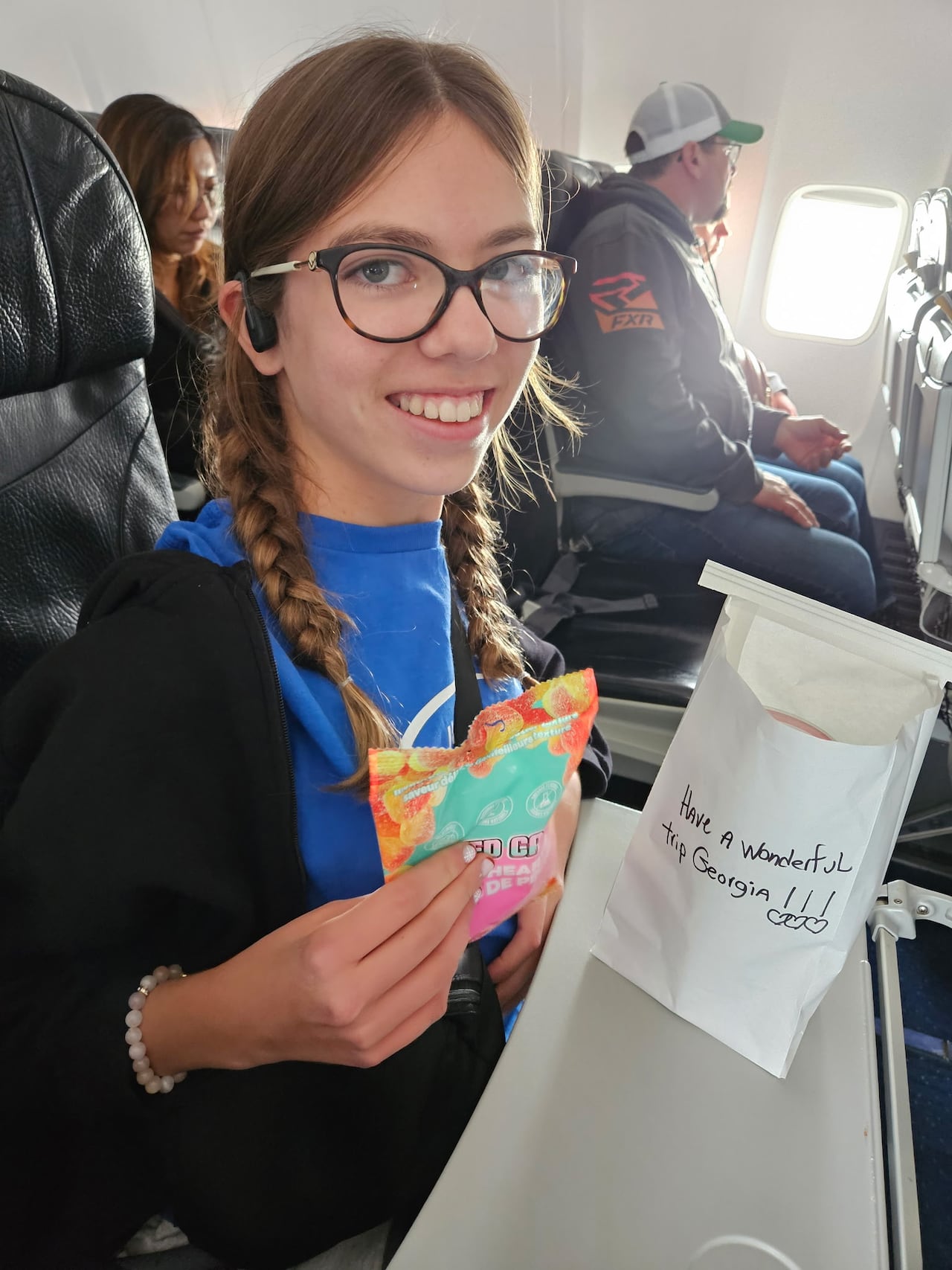 A girl with braided hair smiles while sitting on an airplane