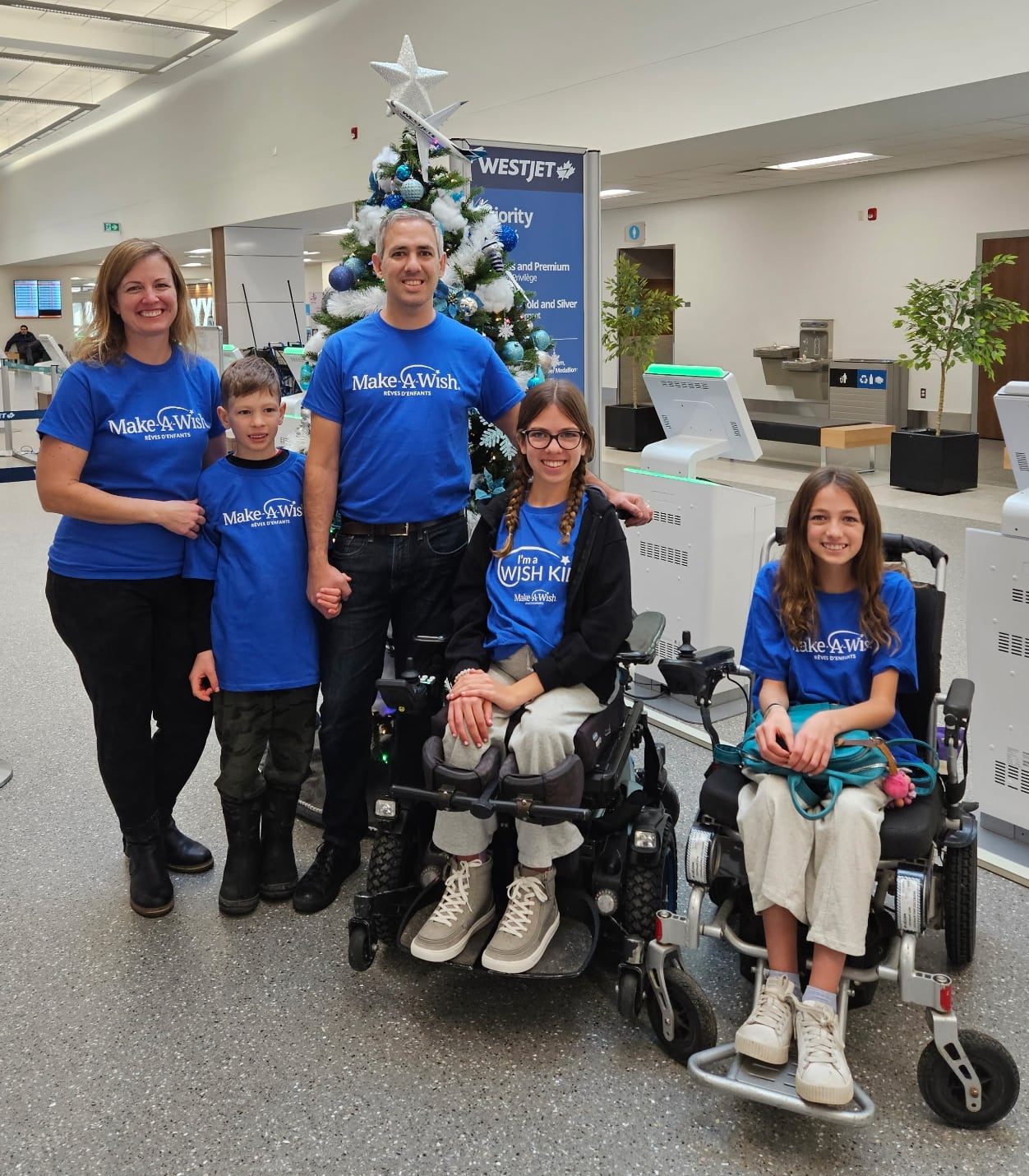 Two girls in wheelchairs with a little boy and two adults in an airport with matching blue shirts