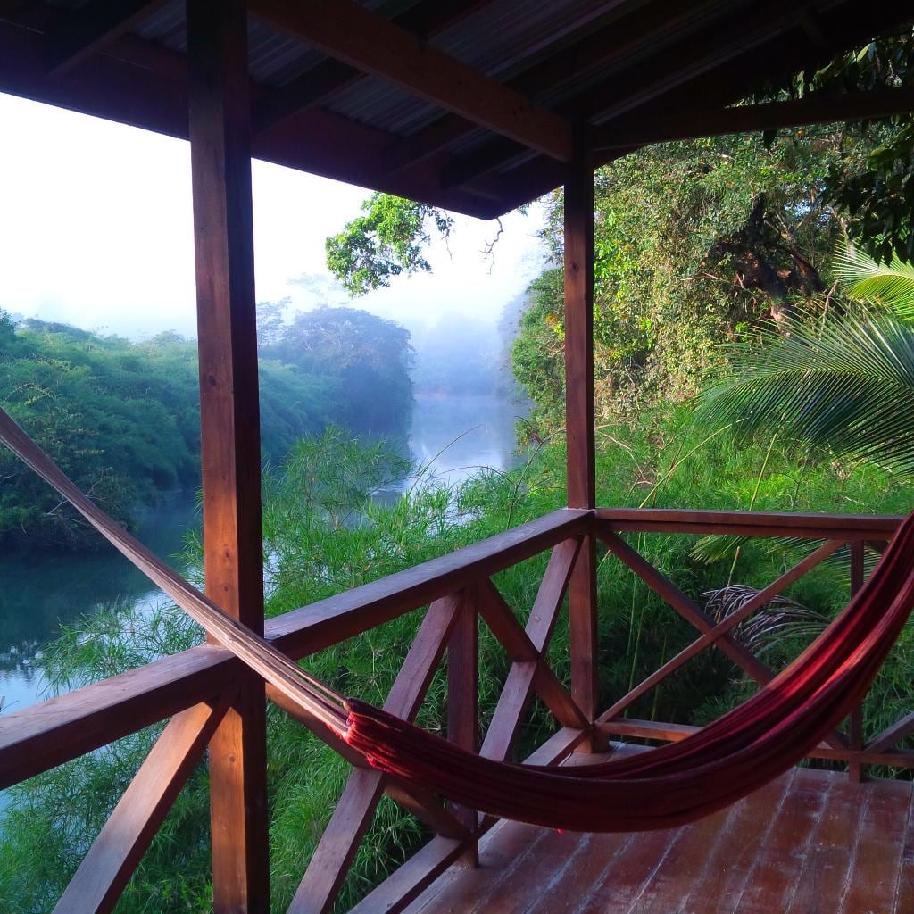 A hammock stretches across a balcony next to a small river.