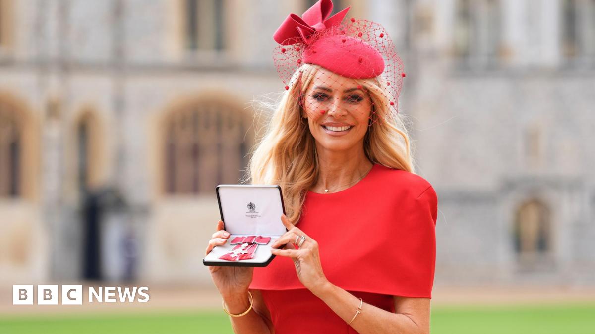 Tess Daly holds her medal after being made a Member of the Order of the British Empire (MBE) at an investiture ceremony at Windsor Castle. She wears a red dress and a fascinator.