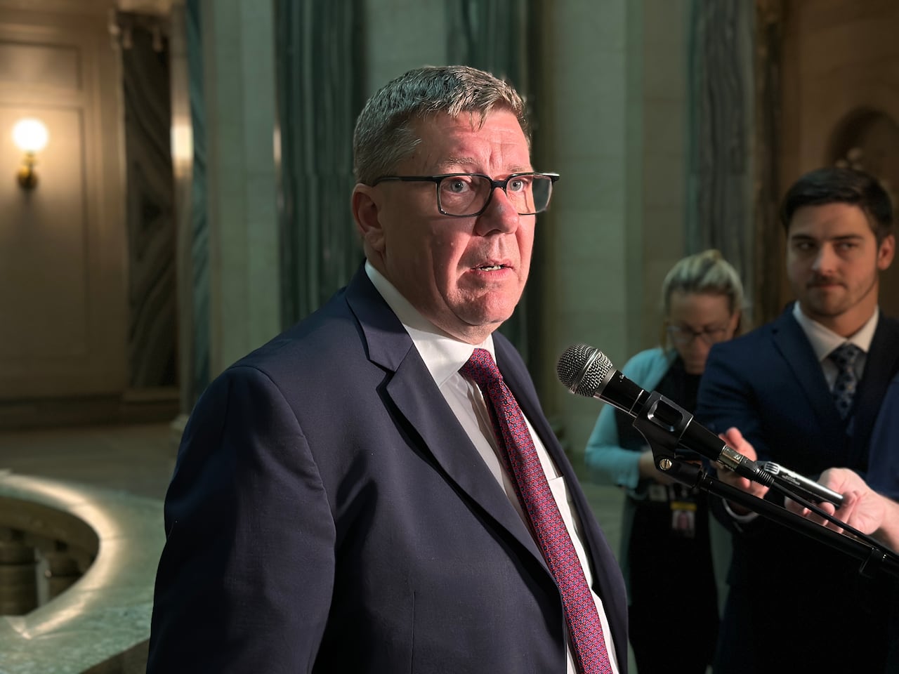 A man in a navy suit speaks into a microphone.