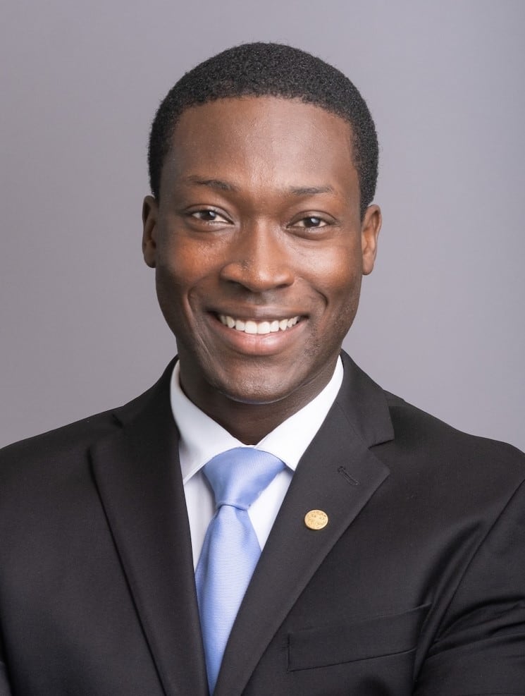 A man in a suit with a blue tie poses for a studio photo