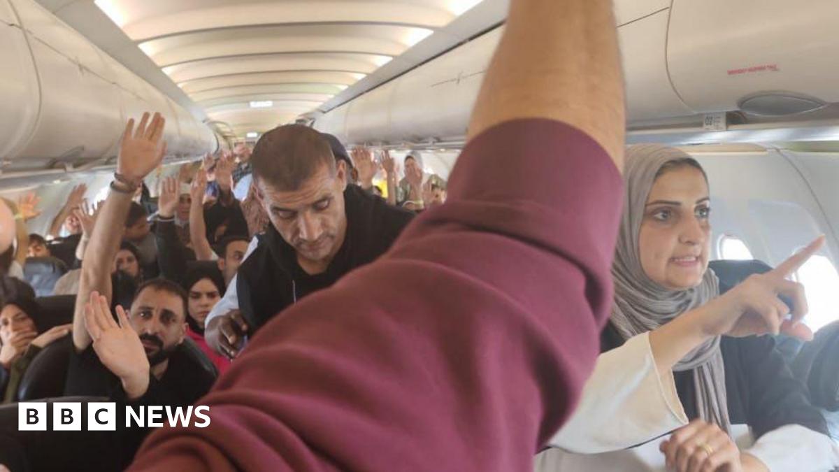 Passengers, including men and women,  raise their hands in a plane