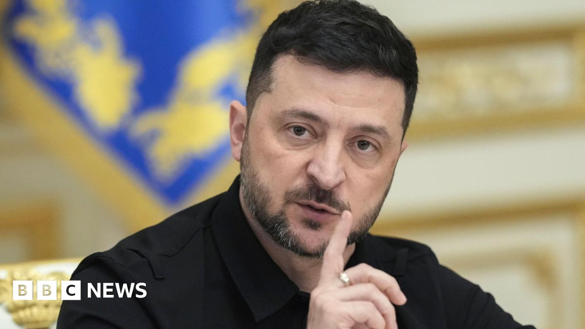 Ukrainian President Volodymyr Zelensky wears his customary black shift and holds his index finger in front of his face.