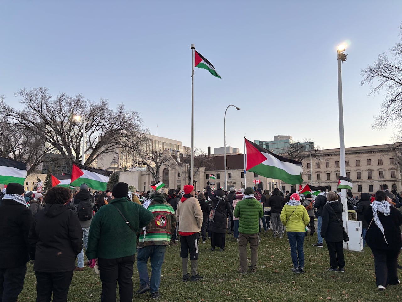 A large group of people wearing coats stand waving black, white, green and red flags