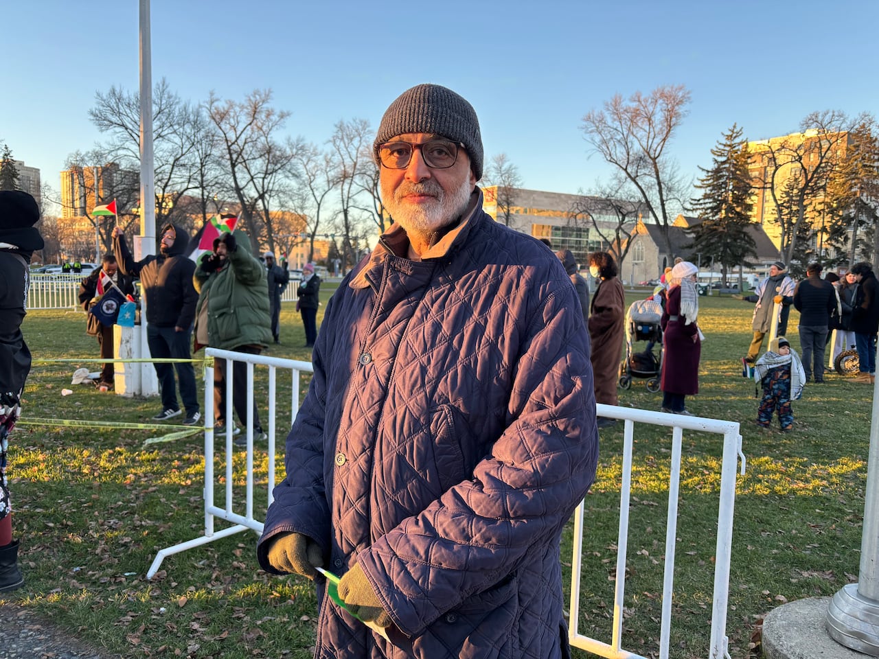 Man with white beard and dark eyeglasses wears a grey hat and a dark blue coat 