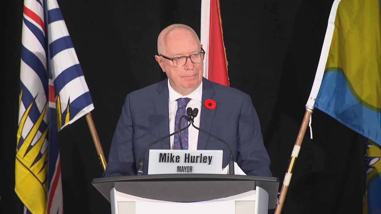 A bald man in a suit speaking in front of a podium.