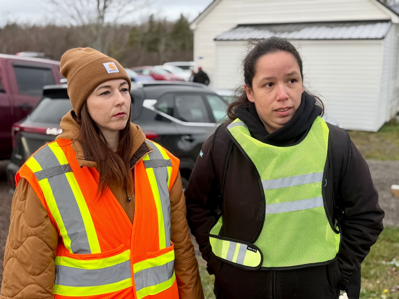 Two women in safety vests stand in front of a white building.