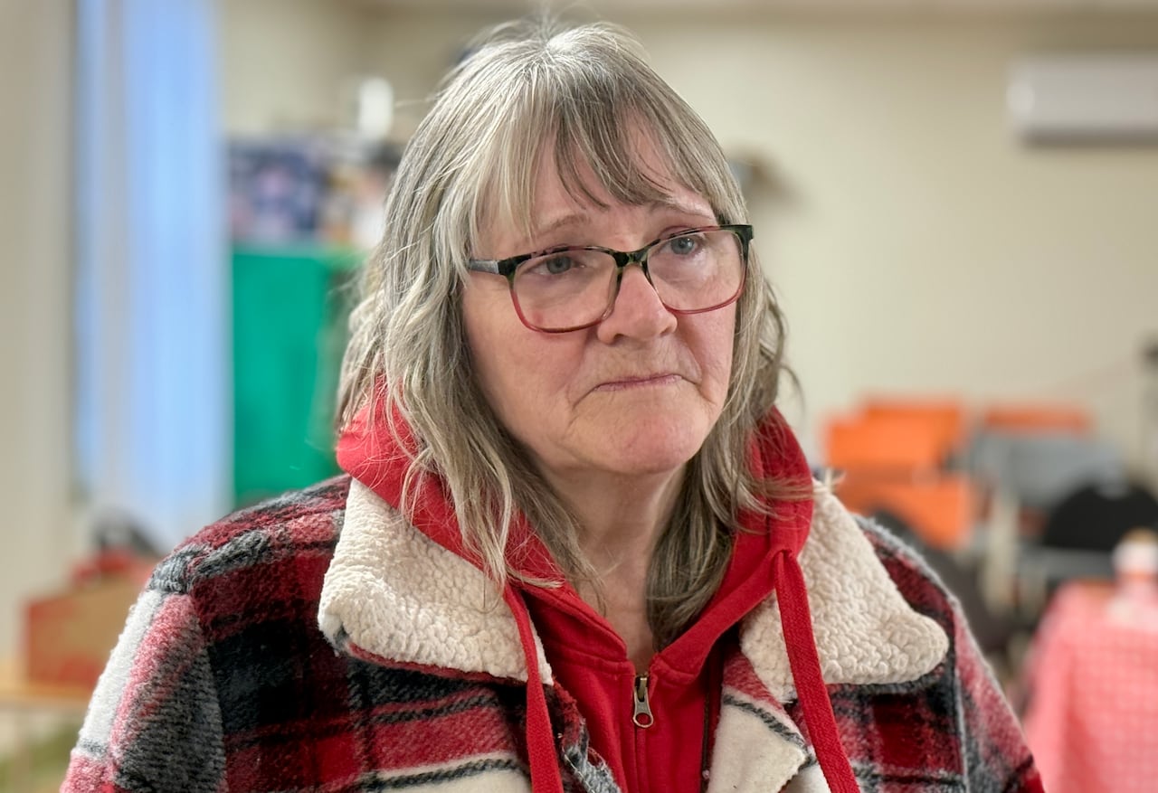 A woman in a red plaid coat with glasses and grey hair.