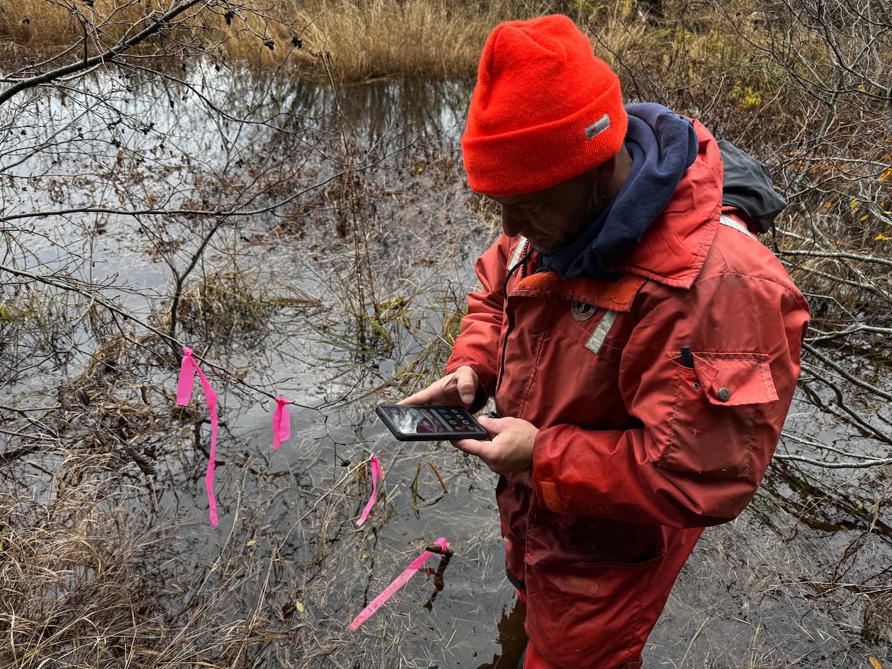 A man in an orange rain suit stands in water with his cell phone.