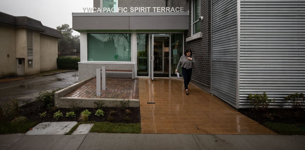 A woman exits an apartment building with the words 'YWCA Pacific Spirit Terrace'.