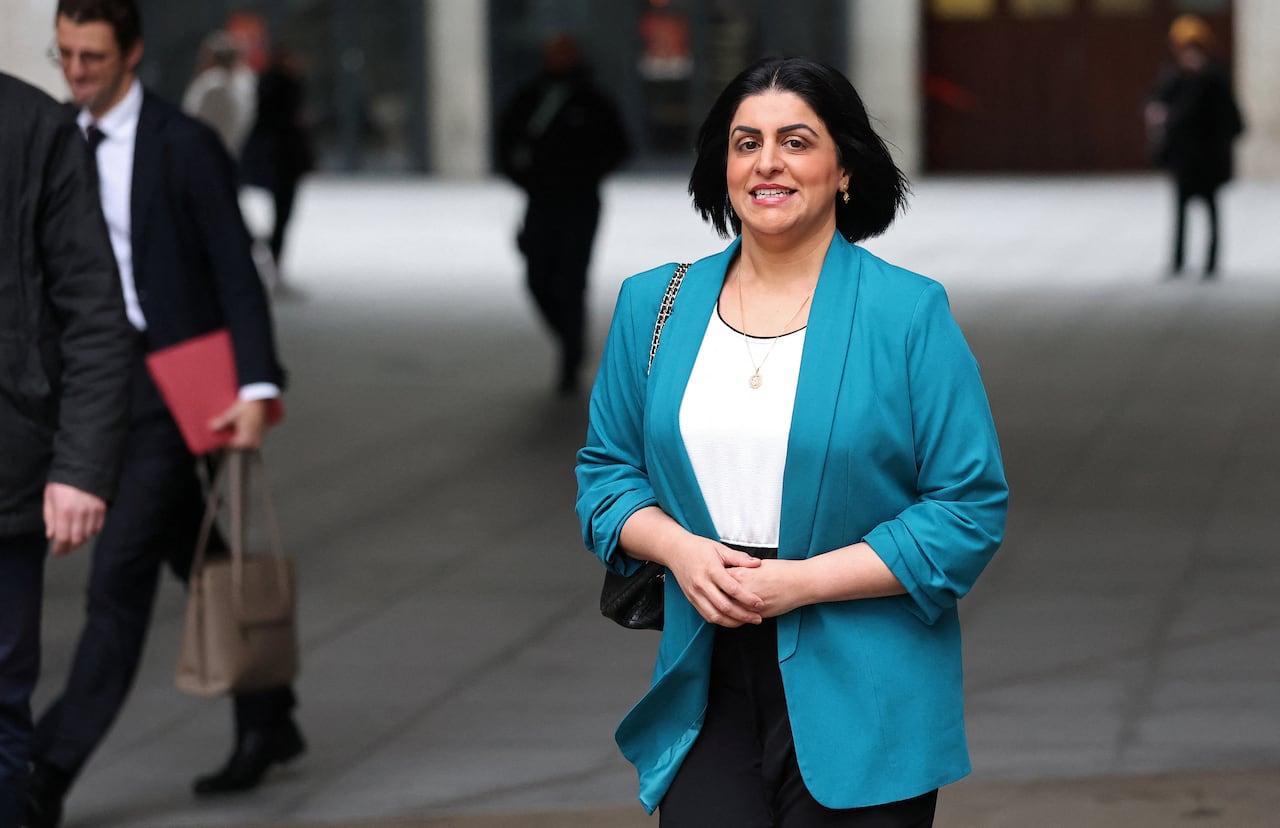 A woman in a teal blazer walks outside a building.