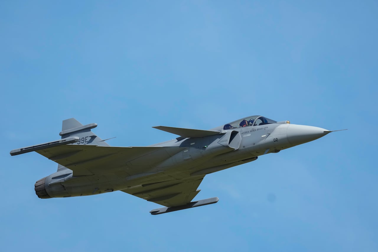 A fighter jet flies in the air in front of a clear blue sky.